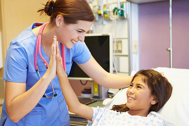 A smiling nurse in scrubs high fives a young patient in a hospital bed.