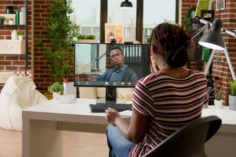 A client talks with a smiling counselor via teleconference on a laptop.